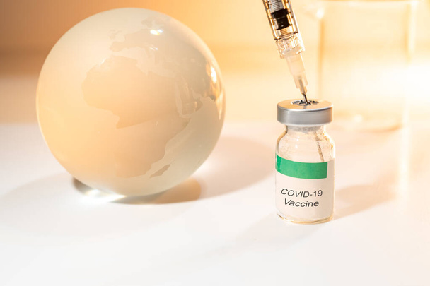 Glazen bol en spuit met Covid-19 vaccin en bekerglas op witte achtergrond. Wereldwijd gezondheidszorgconcept - Foto, afbeelding