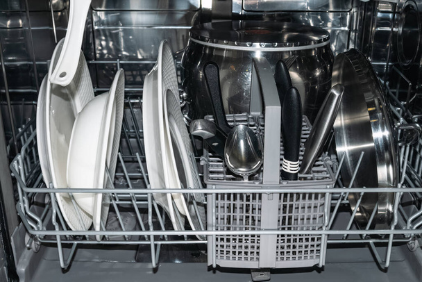 Tiszta fehér lap, tálak, fémserpenyő és evőeszközök mosogatógépben - Fotó, kép