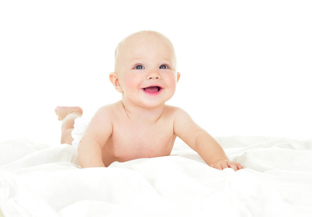 Beautiful smiling baby lying on his stomach in bed. One, isolated on white. - Фото, изображение