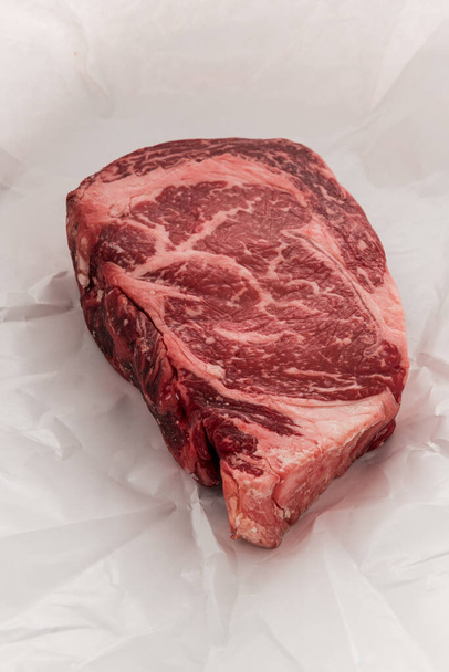 A raw New York strip Ribeye steak thick steak on paper that its wrapped in when bought fresh from a store. - 写真・画像