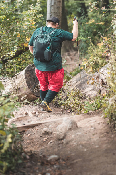 Una persona con sobrepeso grave está descendiendo por la montaña usando bastones de senderismo. Concepto foto de un hombre que pierde peso mientras camina por las montañas. - Foto, imagen