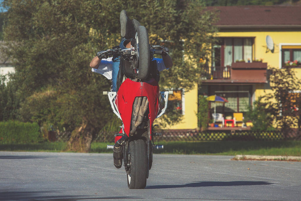 Motorrad-Stuntman übt auf einem Heimparkplatz auf einem rot-weißen Motorrad. Frontalansicht eines Stuntmans, der einen Wheelie auf einem Motorrad macht. - Foto, Bild