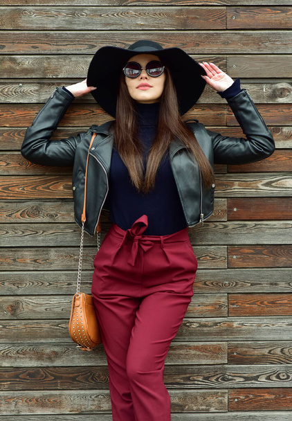 Beautiful brunette woman in sunglasses and in a hat  over wooden background. Street fashion. Outdoors. - Photo, image