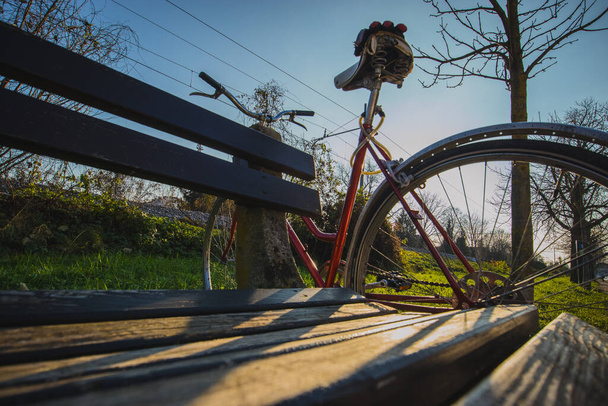 秋の晴れた日に公園の木のベンチの横に駐車した赤いヴィンテージの自転車. - 写真・画像