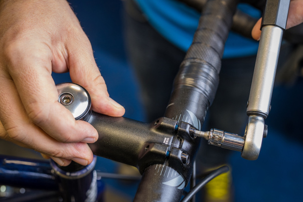 Anziehen eines Fahrradlenker-Vorbaus mit einem kleinen Drehmomentschlüssel. Richtige Art und Weise, einen Fahrradlenker festzuziehen. Fahrradservice in der Werkstatt. - Foto, Bild