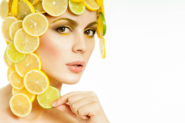 Piękna kobieta z soczystymi cytrynami i limonkami we włosach. Idealna skóra. Profesjonalny makijaż. Piękna kobieta w kapeluszu owoców. - Zdjęcie, obraz