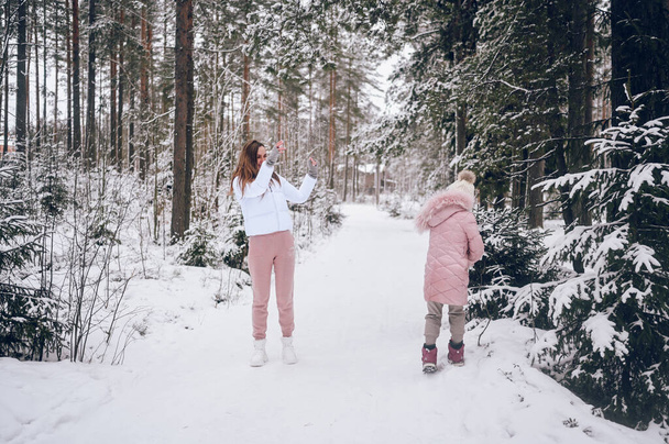 Onnellinen äiti ja pieni söpö tyttö vaaleanpunainen lämmin outtwear kävely pelaa lumipallo taistelu hauskaa luminen valkoinen talvi havumetsässä kuusen metsässä ulkona. Perhe urheilu loma toiminta - Valokuva, kuva