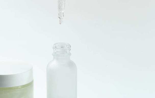 White transparent cosmetic bottle and pipette with drop of oil serum liquid essence on white background, cosmetics laboratory, dropper and hygiene  - Foto, imagen
