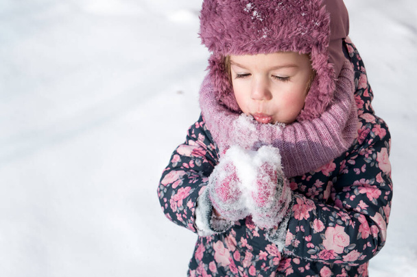 Winter, games, family, childhood concepts - close-up portrait authentic little preschool minor girl in pink hat warm clothes have fun smiles in cold frosty weather day. Funny kid blow on white snow - Valokuva, kuva