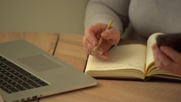 Close-up gerimpelde mannelijke handen schrijven informatie. Oude volwassen vrouw werkt op kantoor, met behulp van computer, handschrift notities - Video