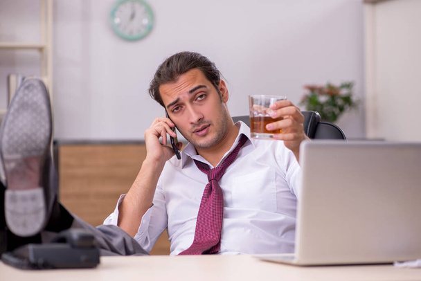 Молодой работник, пьющий алкоголь в офисе - Фото, изображение