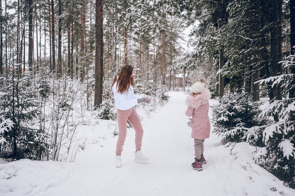 Счастливая мать и маленькая милая девочка в розовой теплой наружной ходьбе, играя в снежки борьбы весело в белоснежном зимнем хвойном лесу с еловыми лесами на открытом воздухе. Отдых в семье - Фото, изображение