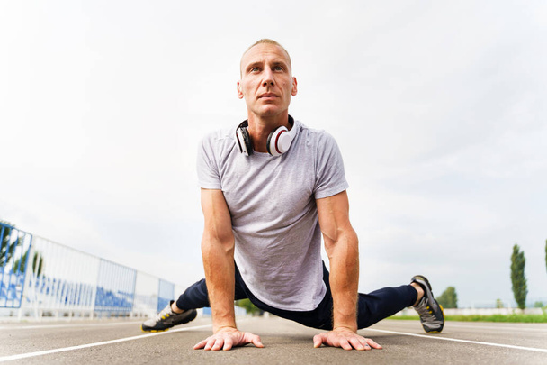 Alacsony látószögű kilátás a felnőtt kaukázusi férfi nyújtózkodik a futópályán - szőke férfi sportoló felkészülés a nyári edzésre - valós emberek egészséges életmód koncepció - Fotó, kép