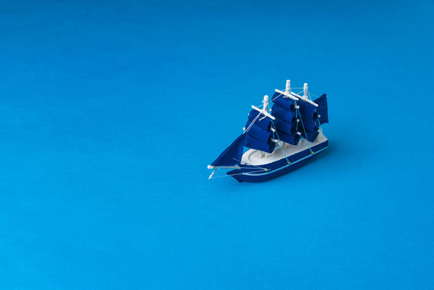 A toy wooden sailboat on a dark blue background imitating the sea. The concept of travel and adventure. - Foto, immagini