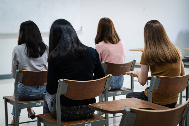 Young female university students concentrate on doing examinations in the classroom. Girl students seriously write the exercise of the examinations in the classroom. - Photo, Image