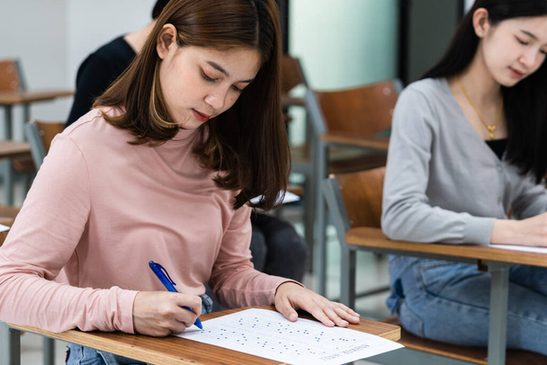 Young female university students concentrate on doing examinations in the classroom. Girl students seriously write the exercise of the examinations in the classroom. - Photo, Image