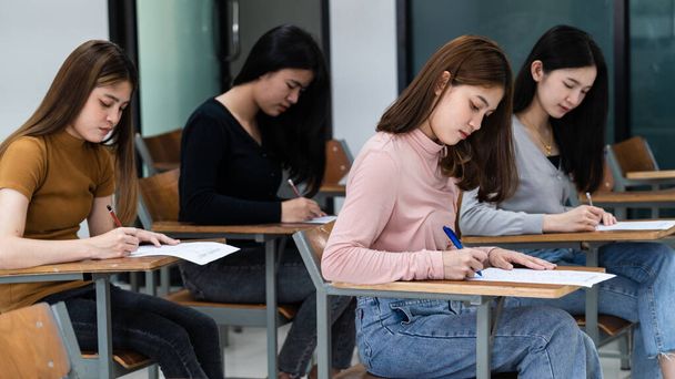 Junge Studentinnen konzentrieren sich darauf, im Hörsaal Prüfungen abzulegen. Schülerinnen schreiben die Prüfungsaufgaben ernsthaft im Klassenzimmer. - Foto, Bild