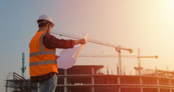 Inżynieria azjatycka nosząca twarde kapelusze i trzymająca plan prac budowlanych na budowie - Zdjęcie, obraz
