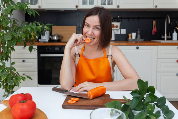 Young beautiful woman sitting at kitchen background while cutting vegetables - Foto, imagen