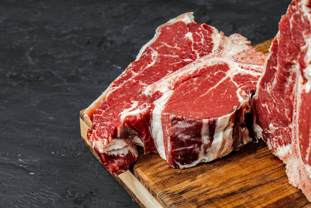Raw T-bone steak cooking on stone dark table. - Zdjęcie, obraz