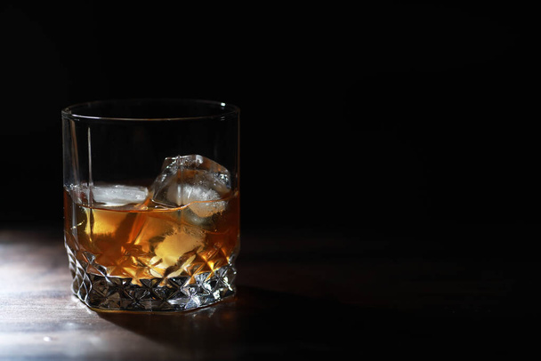 Стакан крепкого алкогольного напитка со льдом на деревянной барной стойке. Виски со льдом. Стекло с охлажденным напитком. - Фото, изображение