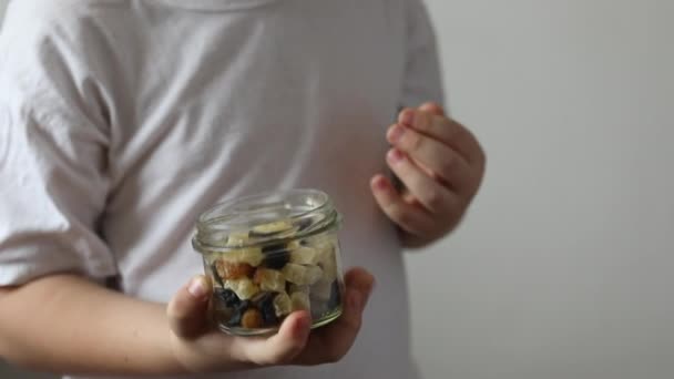 De jongen bijt droog fruit uit glas. Het concept van de juiste voeding, gezonde snacks. - Video