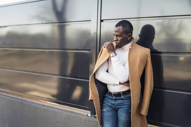 A shallow focus shot of a stylish handsome African male in a coat posing for the camera - Фото, изображение