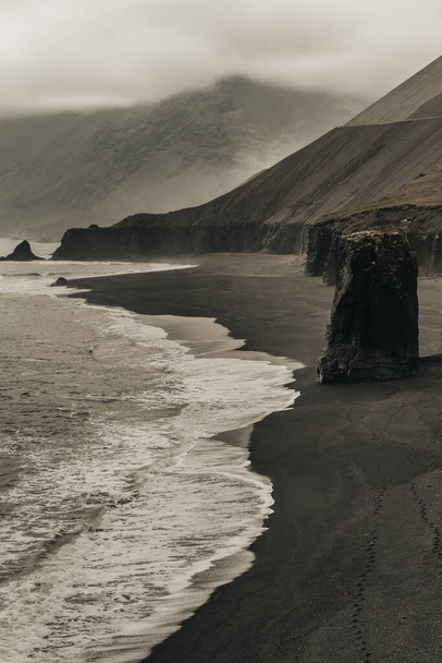 A greyscale shot of a beach with wavy ocean and sandy mountains with black sand in Iceland - Foto, immagini