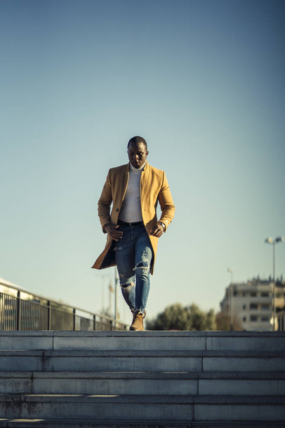 Pionowe ujęcie przystojnego afrykańskiego mężczyzny w płaszczu schodzącego po schodach - Zdjęcie, obraz