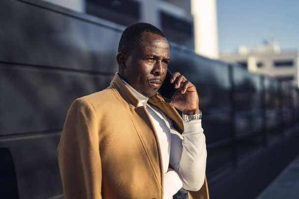A shallow focus shot of a stylish handsome African male in a coat talking by phone - Фото, зображення