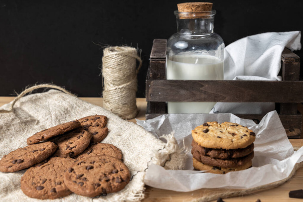A closeup shot of delicious chocolate chip cookies (galletas), milk in a jar, and jute twine - Zdjęcie, obraz