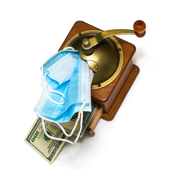 the concept of earning money on a pandemic in a manual coffee grinder medical masks are ground and the output is cash bills on a white background. High quality photo - Photo, Image