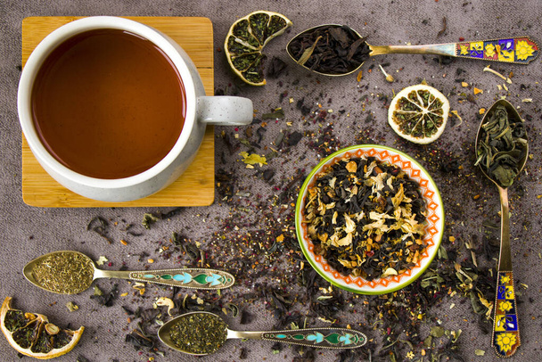 A top view of natural herbal teacups with assorted dried tea leaves and a collection of vintage spoons - Foto, immagini