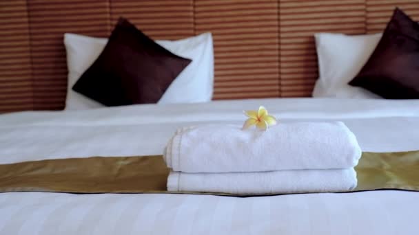 Plumeria e asciugamani di fronte alla cameriera dell'hotel che fa il letto nella camera d'albergo di lusso pronta per il viaggio turistico. - Filmati, video