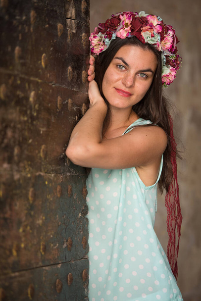 Young woman in blue shirt with flower head band standing by the door, looking into the camera - Photo, Image