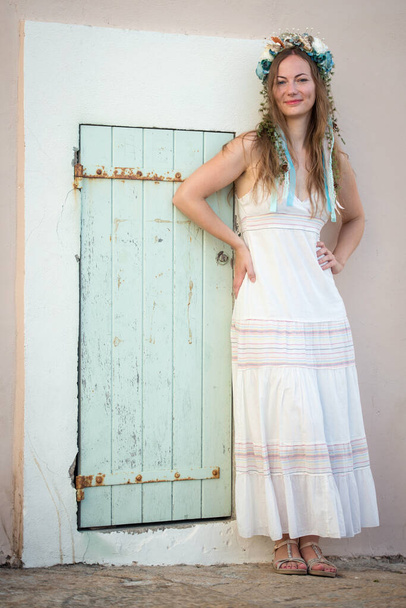 Young woman in white dress with flower head band standing by the door - Photo, Image