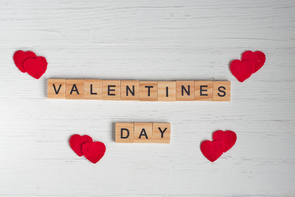 「バレンタインデー」という言葉のトップビューは、古い白い木製の背景に正方形の木製のタイルと赤の小さな心からレイアウト. - 写真・画像