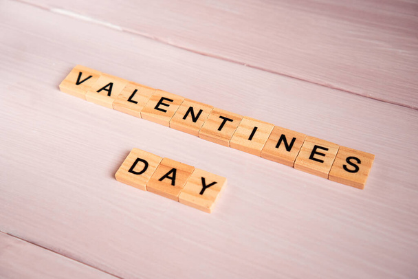 Word valentines day laid out from square wooden tiles on pink wooden background. - Zdjęcie, obraz