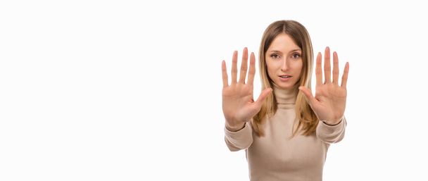 I say no. Serious blond girl keeps palms of both hands forward at camera, makes forbid sign, restricts or warns, extends arms in stop sign. Studio shot, white background. Place for ad - Photo, Image