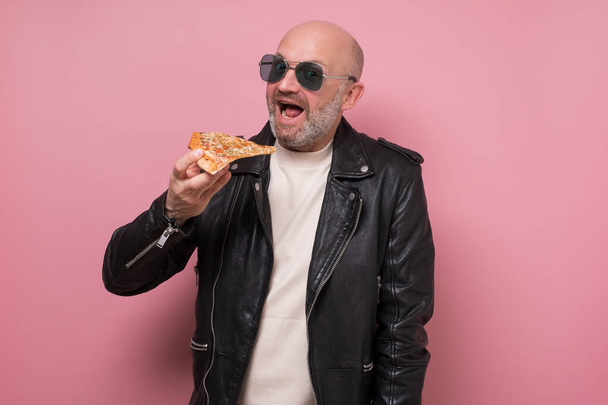 Веселый парень ест пиццу на розовом фоне - Фото, изображение