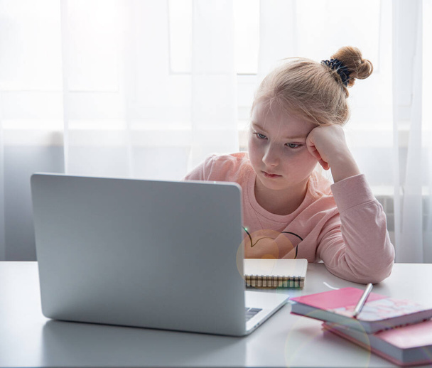 Távolsági oktatás. Egy iskoláslány, aki házi feladatot tanul otthon, az interneten keresztül. Társadalmi távolság karantén alatt - Fotó, kép