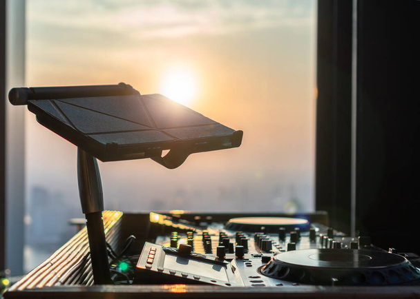 Contrôleur DJ Disc Jockey pour la fête sur le toit, le dîner au restaurant de luxe et le divertissement audio en boîte de nuit sur fond de coucher de soleil avec tablette numérique de fichier musical - Photo, image