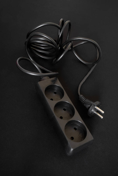 A black power strip for three European outlets lies against a dark background. Close-up - Photo, Image