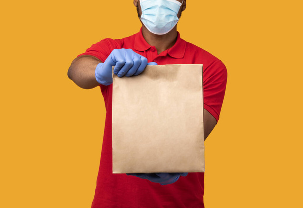 Repartidor negro en máscara médica y guantes que sostienen el paquete - Foto, imagen