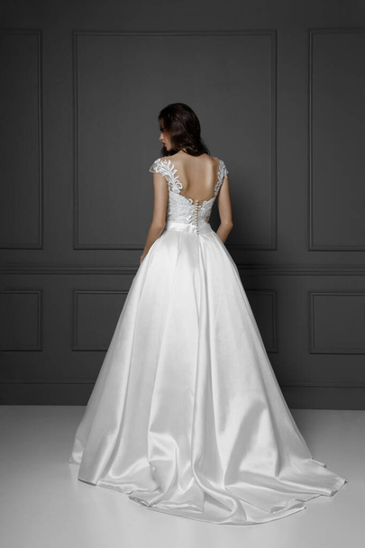 Vista posterior de una tierna modelo morena en blanco delicado vestido de novia princesa, aislado sobre un fondo gris. - Foto, Imagen