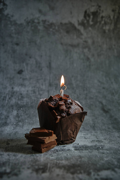 chocolate muffins on a dark background with a lit candle - Photo, Image