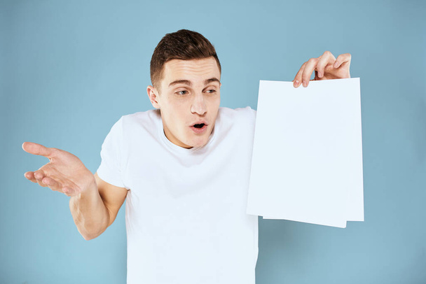 man holding a sheet of paper in his hands white t-shirt cropped view blue background - Photo, image