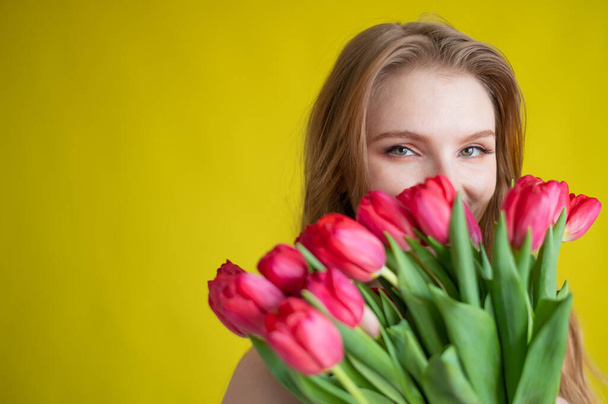 Woman with a bouquet of red tulips on a yellow background. Happy girl in a black dress holds an armful of flowers . Gift for Valentines Day. The most romantic day of the year. - Fotó, kép
