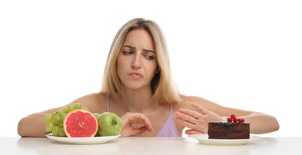 Woman choosing between cake and healthy fruits at table on white background - Φωτογραφία, εικόνα