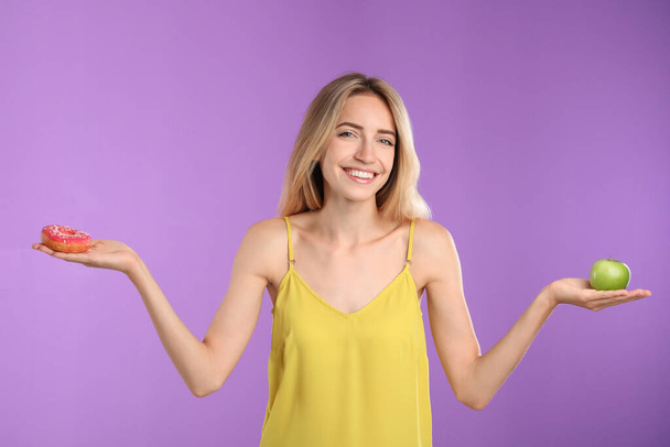 Woman choosing between doughnut and healthy apple on violet background - Photo, image